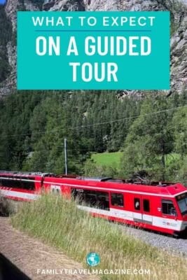 A red Rhaetian Railway train travels through the Swiss Alps, flanked by steep rocky mountains.