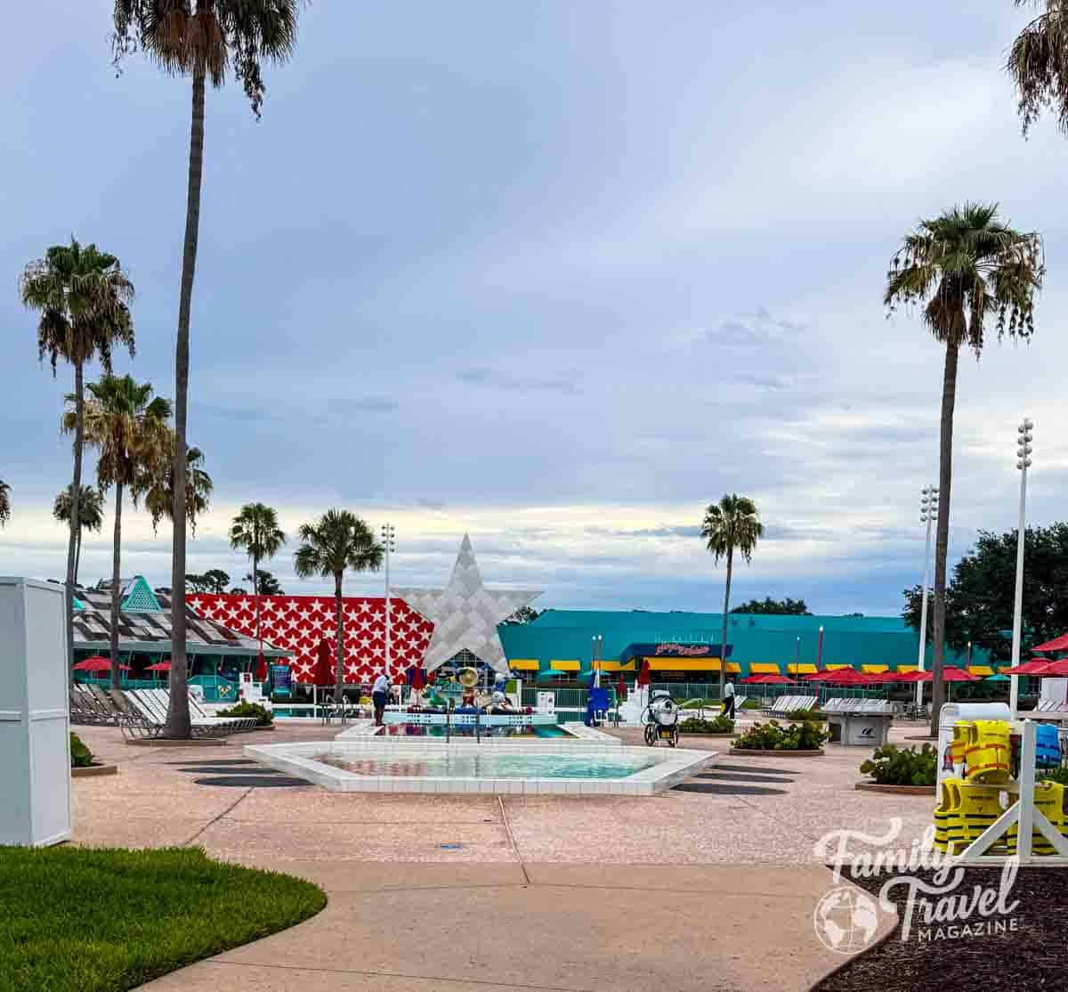 Calypso Pool area at Disney’s All-Star Music Resort with palm trees, fountain, lounge chairs, and colorful resort buildings
