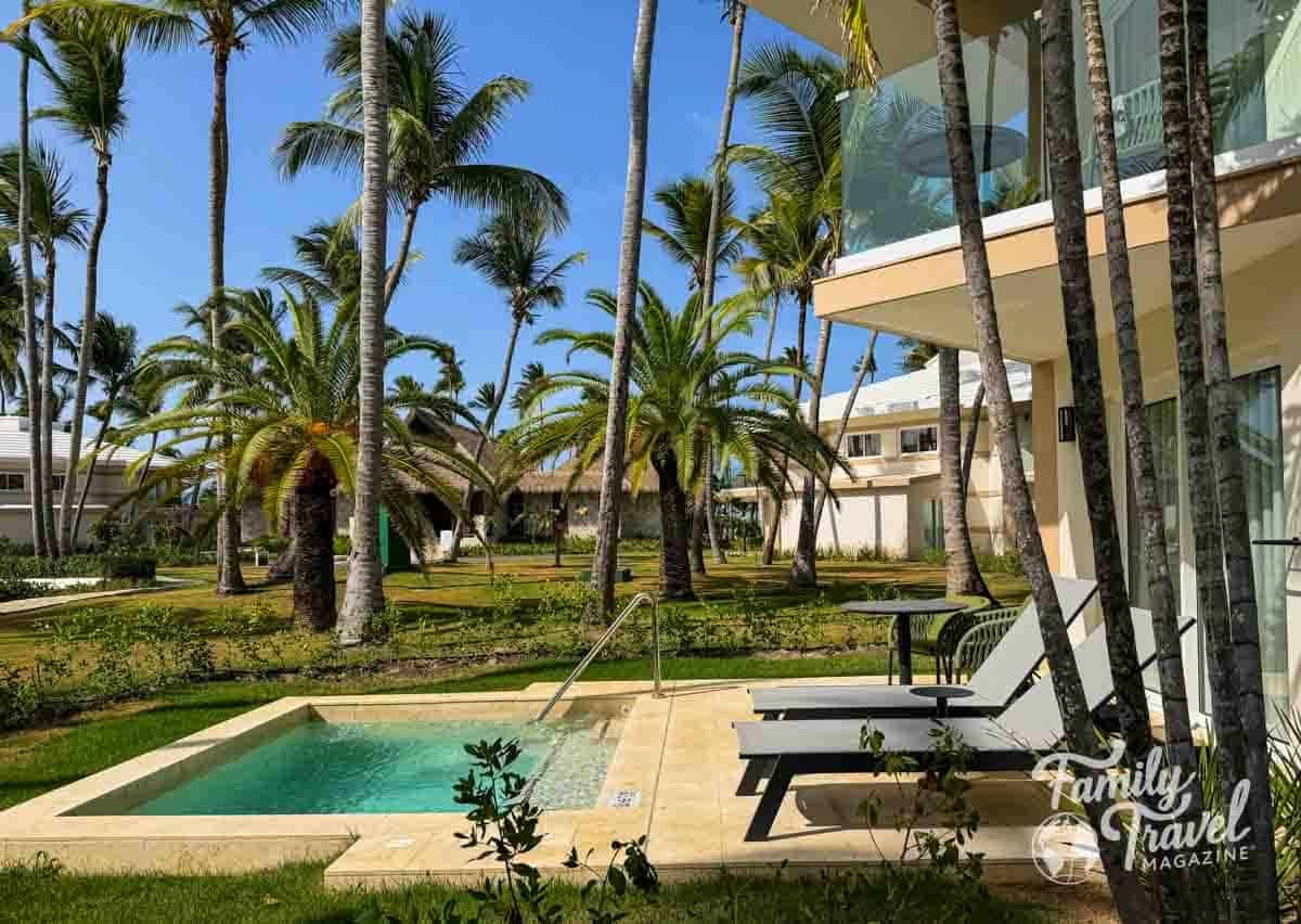 A luxurious tropical resort suite with a private plunge pool, lounge chairs, and numerous palm trees.