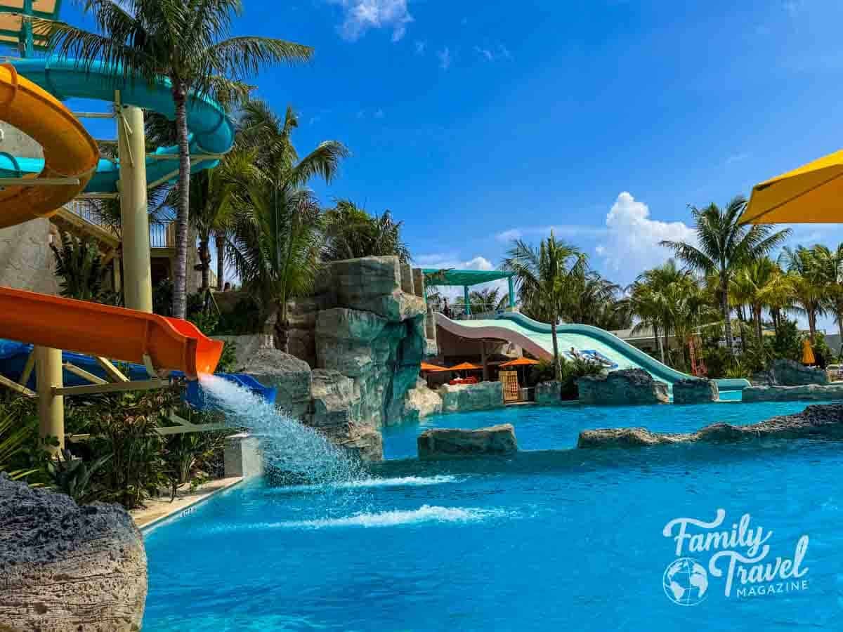A water park features colorful slides, a pool with rock formations, and palm trees under a bright blue sky at Great Tides Waterpark