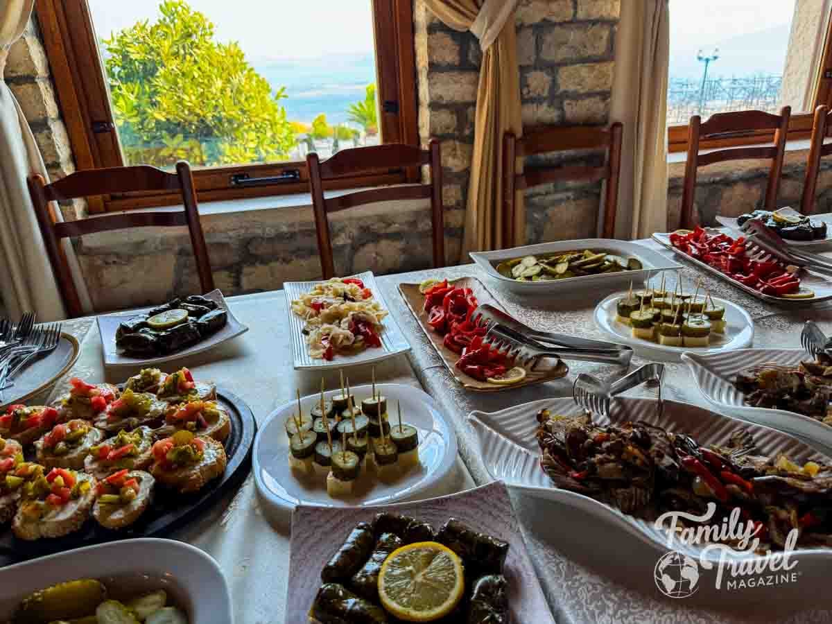 A table is set with various appetizers and small plates in a room with large windows overlooking a landscape.