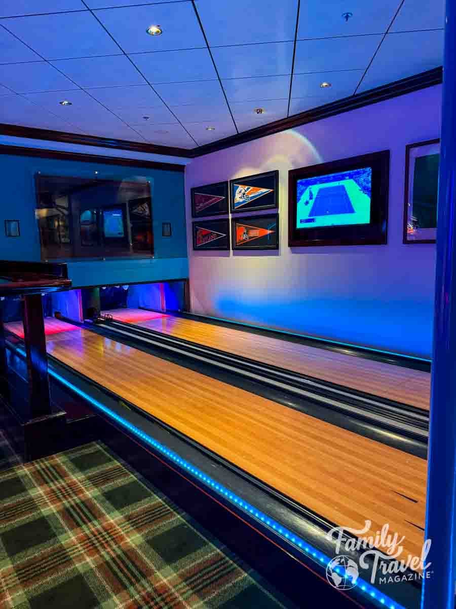 A two-lane bowling alley features blue accent lighting and framed sports pennants on the wall.
