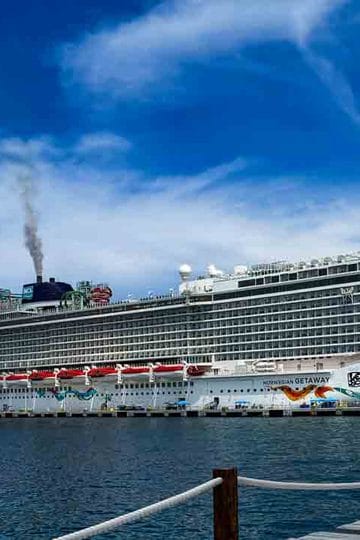 A large cruise ship is docked at a pier under a blue sky with light clouds.
