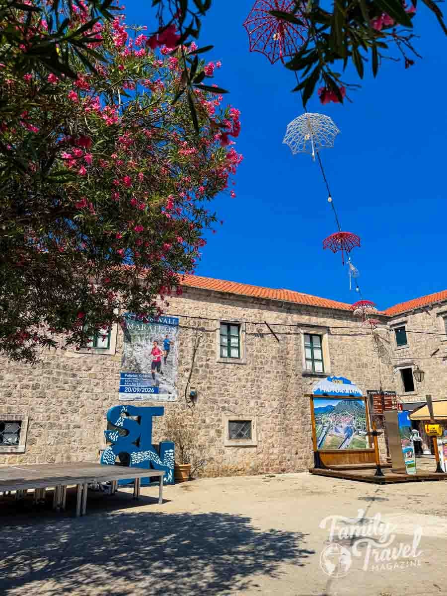 A stone building with a marathon poster and decorative umbrellas hanging from wires against a clear blue sky.