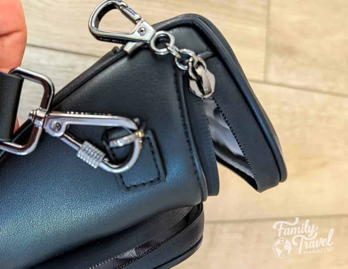 A hand holds a black bag with silver metal clasps and a zippered opening.