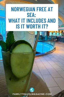 A glass with a cucumber slice and mint garnish sits in front of a blurred indoor atrium